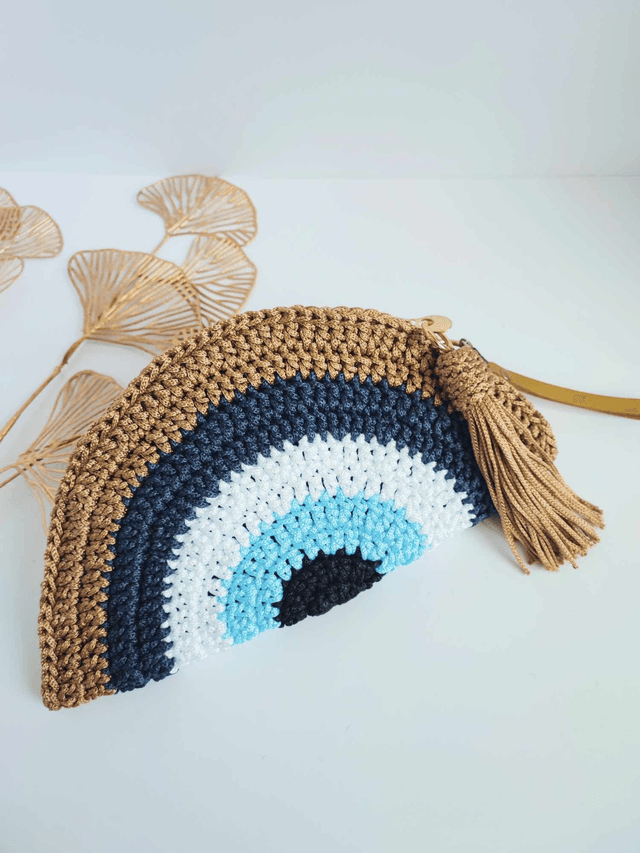Sac Clutch mauvais œil fait main en crochet, pochette Nazar avec dragonne dorée, fermeture zippée et pompon – accessoire artisanal en polyester