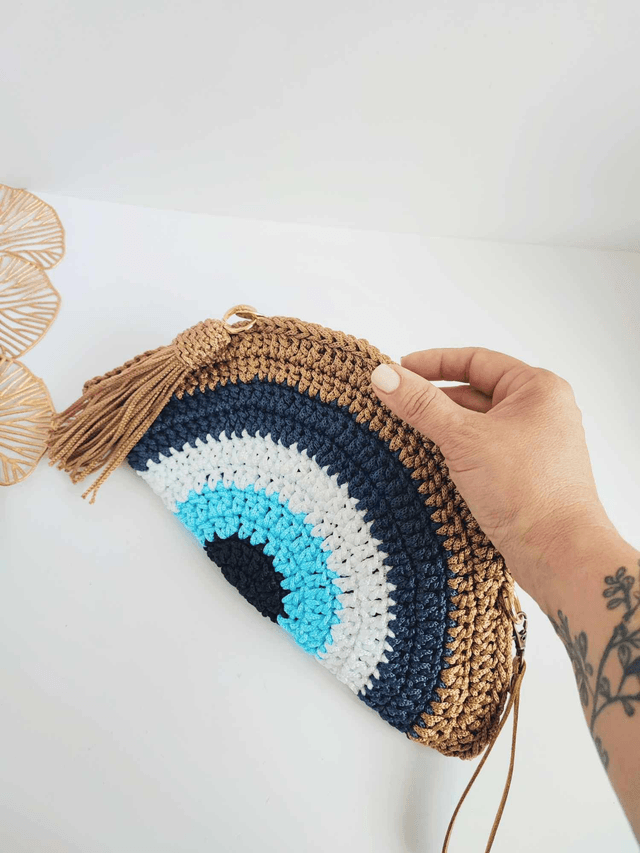Sac Clutch mauvais œil fait main en crochet, pochette Nazar avec dragonne dorée, fermeture zippée et pompon – accessoire artisanal en polyester